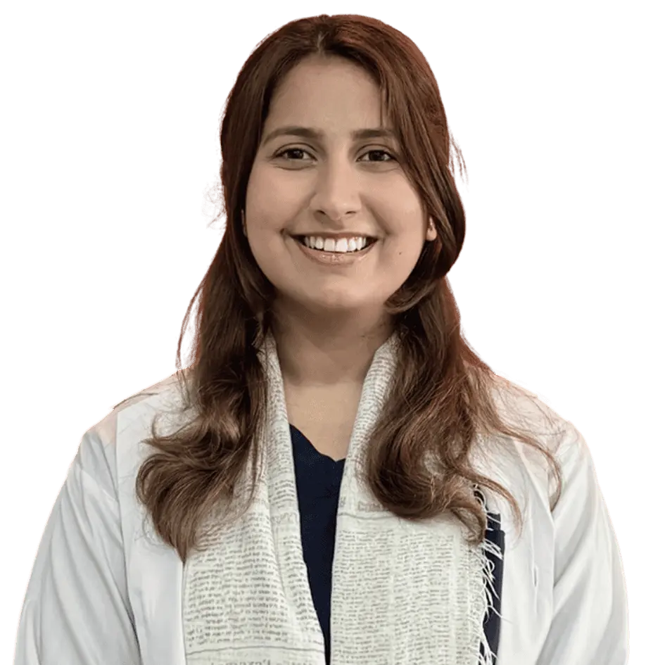 A headshot of a young woman, likely a doctor or medical professional, with long brown hair, smiling brightly. She is wearing a white lab coat and a light-colored patterned scarf over a dark shirt